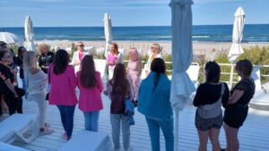 A group of attendees stand on a terrace which overlooks the sea. They are stood together talking.